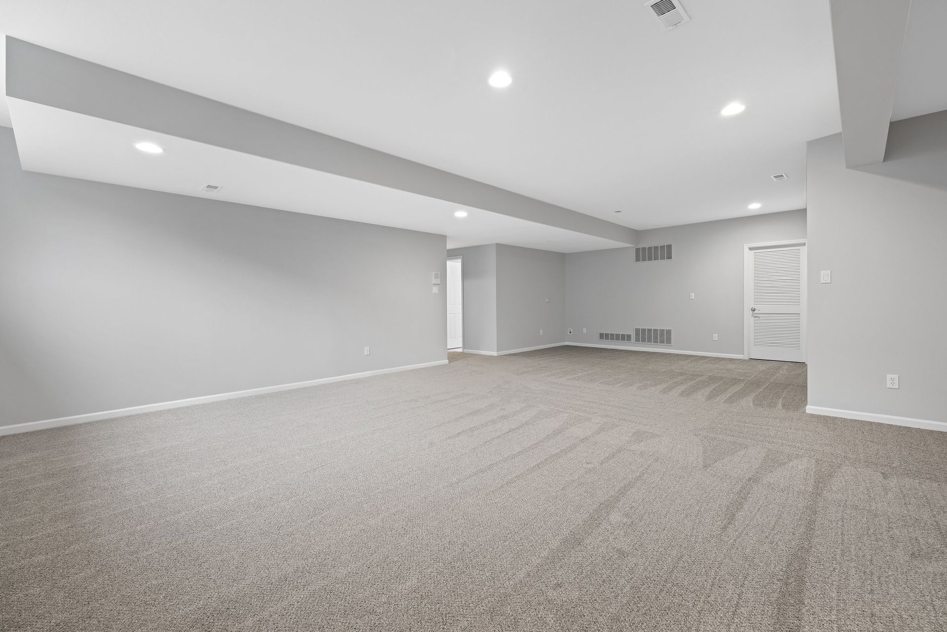 An empty basement with a carpeted floor and white walls.