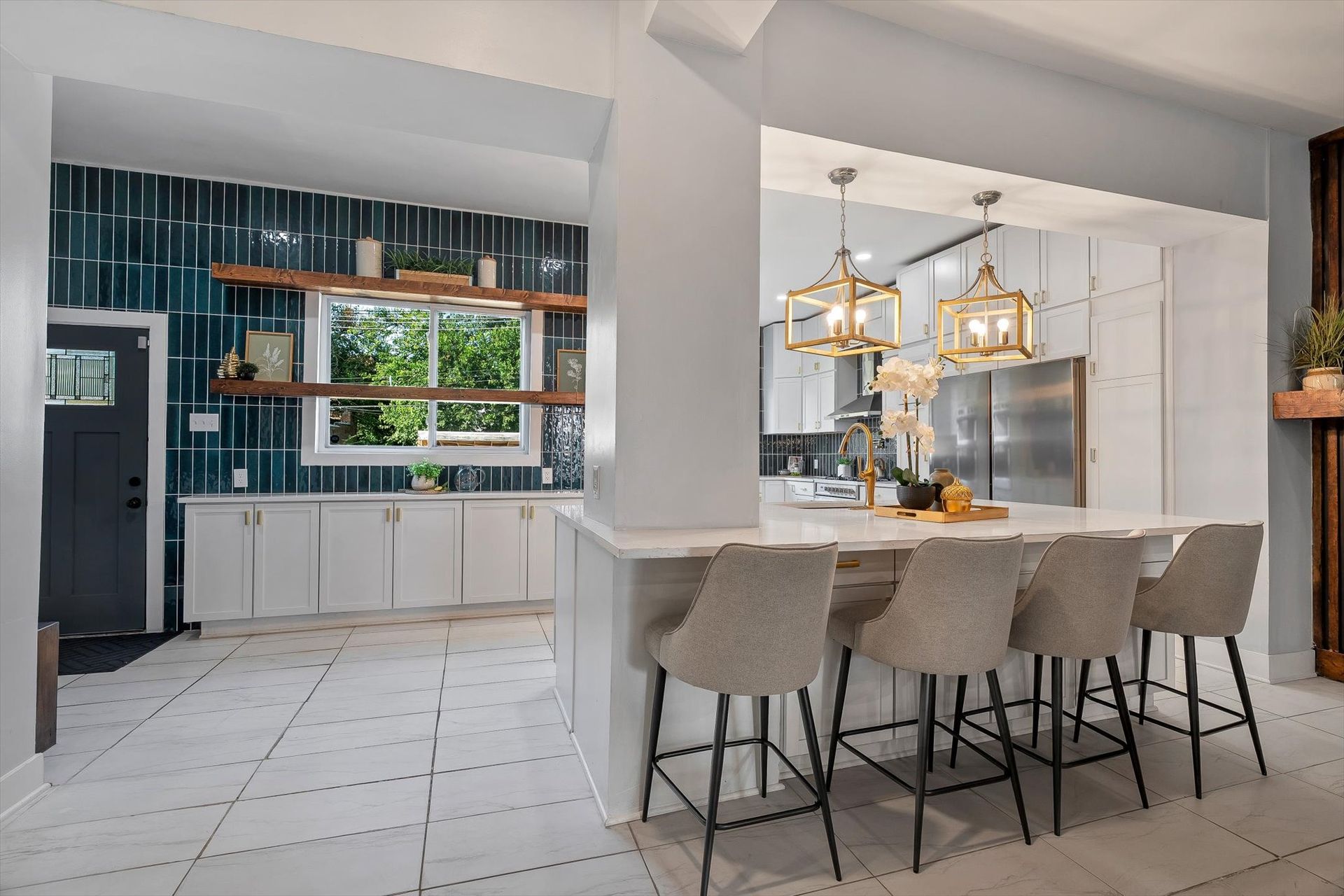 Modern kitchen with white cabinets, teal backsplash, and a breakfast bar with gray stools.
