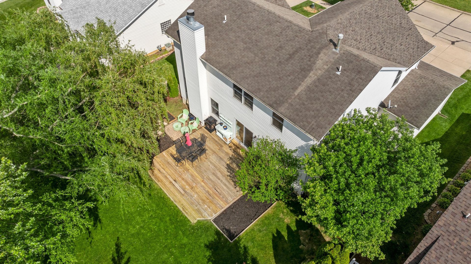 An aerial view of a house with a deck in the backyard surrounded by trees.
