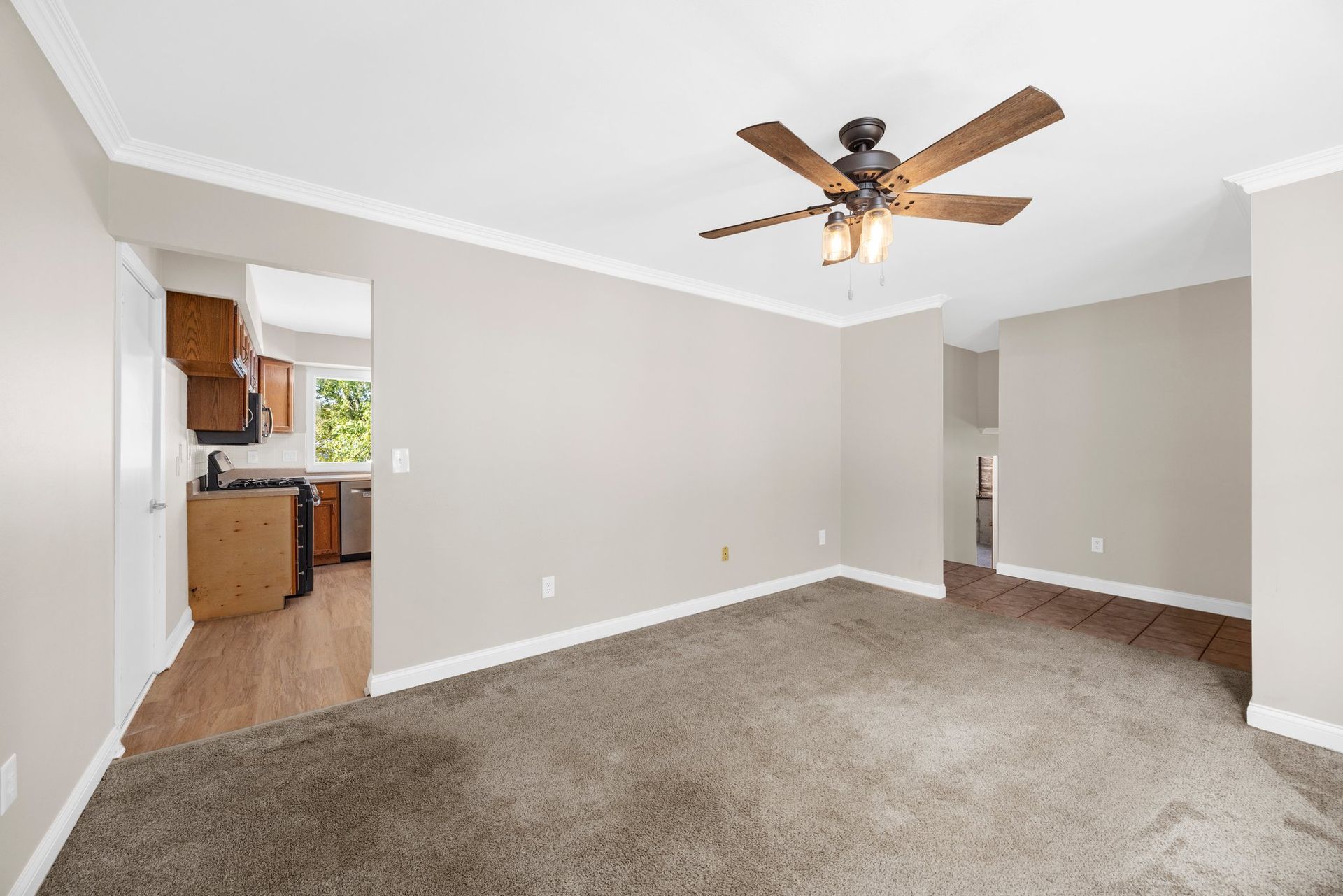 An empty living room with a ceiling fan and a carpeted floor.