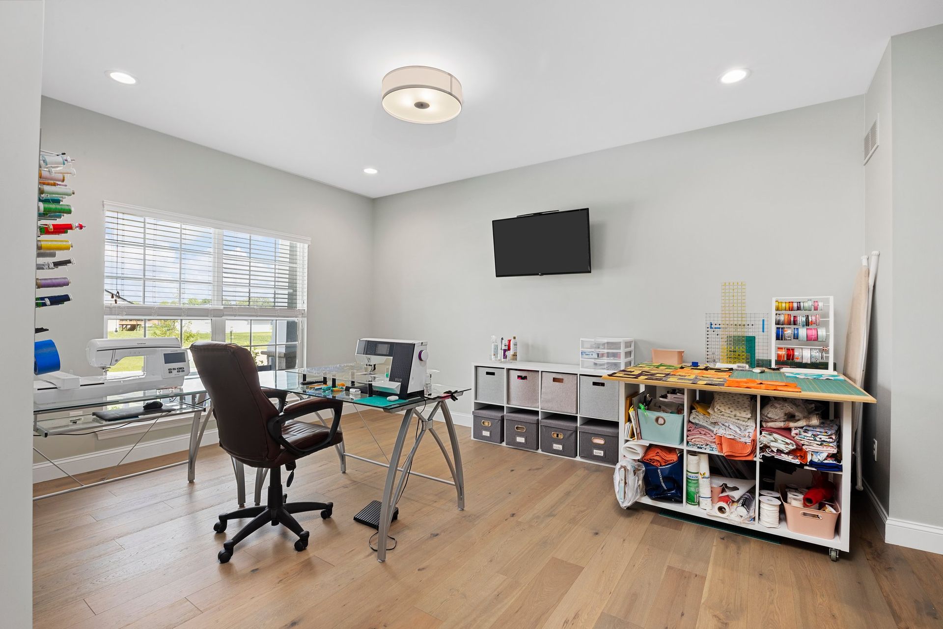 A room with a desk , chair , shelf , and television.