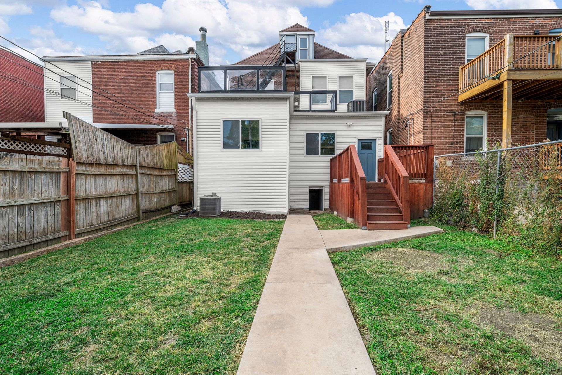 Backyard with white house, red deck, concrete path, and a grassy lawn.
