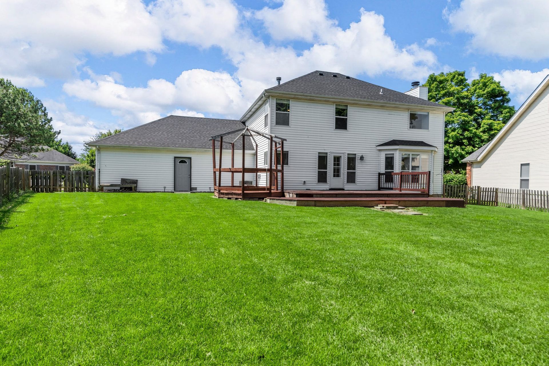 The backyard of a house with a large lush green lawn and a deck.