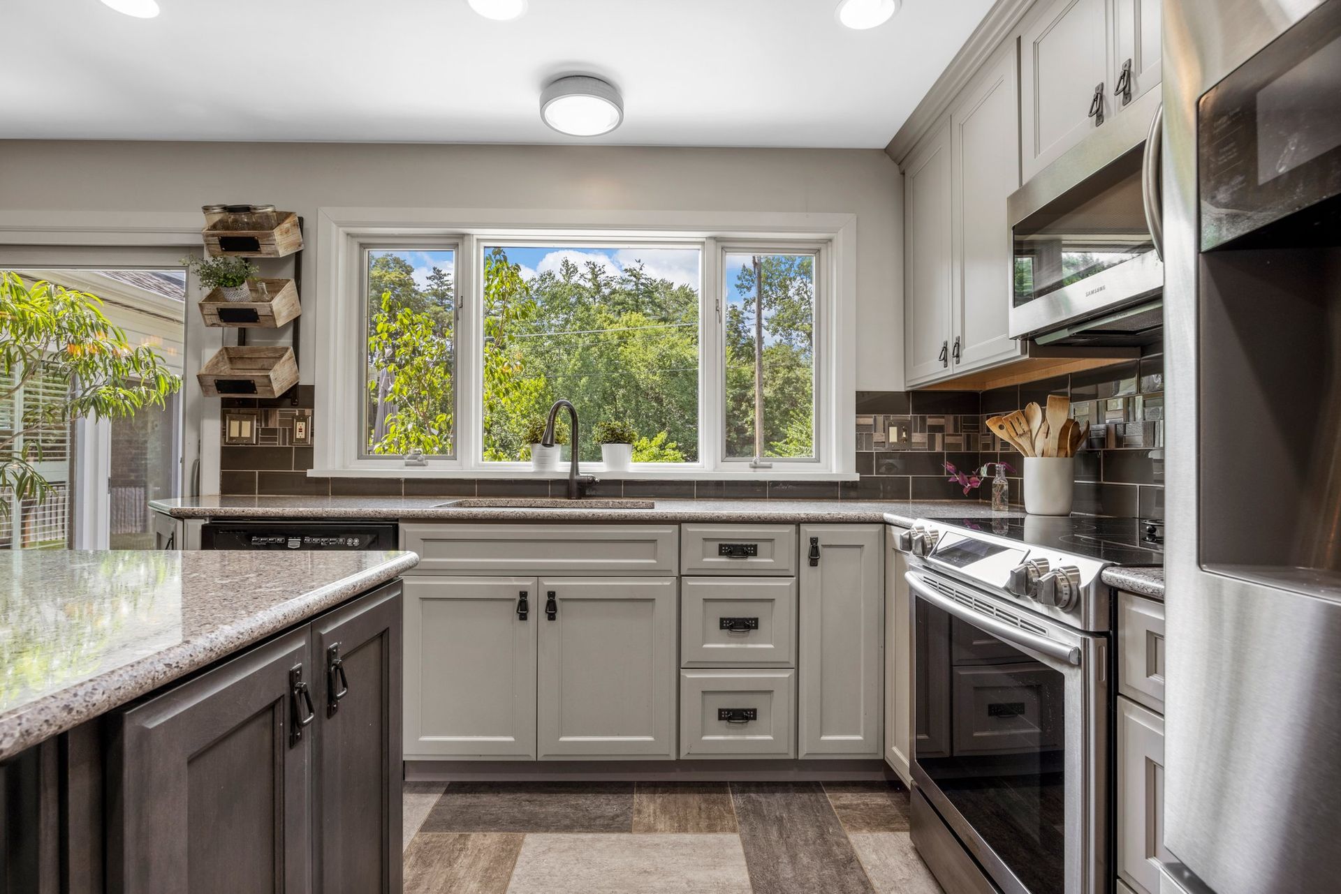 A kitchen with white cabinets , granite counter tops , stainless steel appliances and a large window.