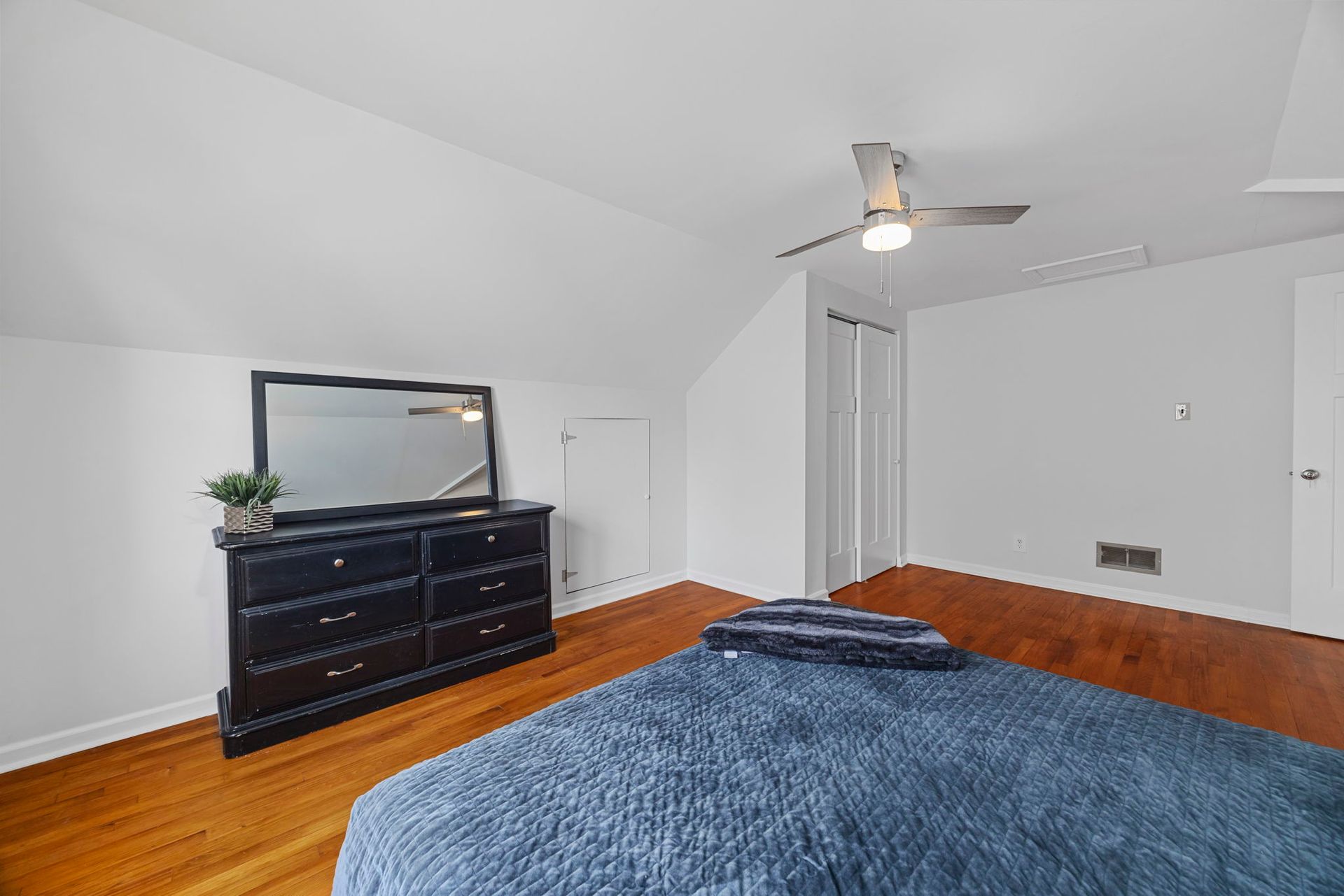 A bedroom with a bed , dresser , mirror and ceiling fan.