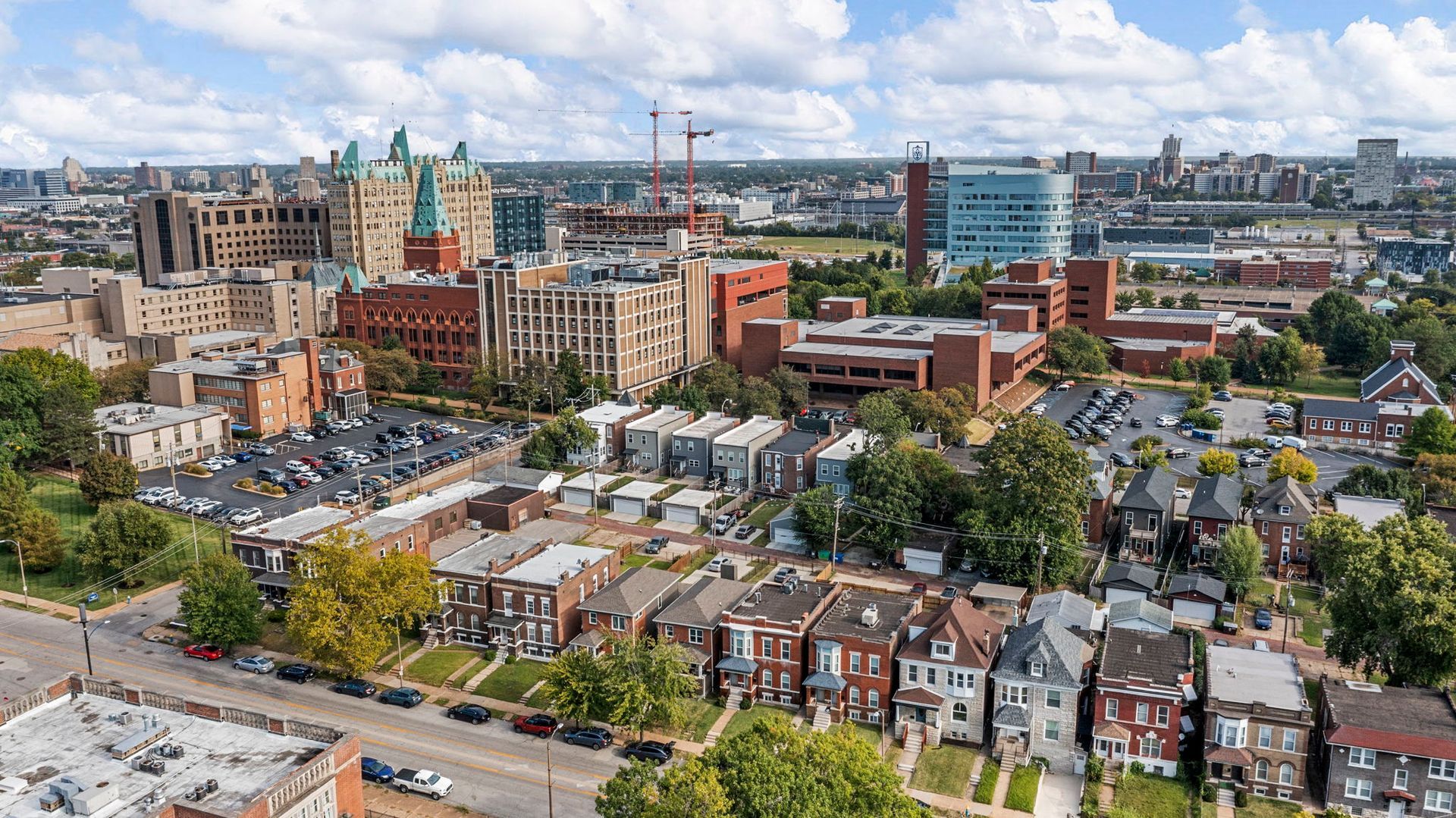 Aerial view: Residential neighborhood with brick houses, trees, and a city skyline