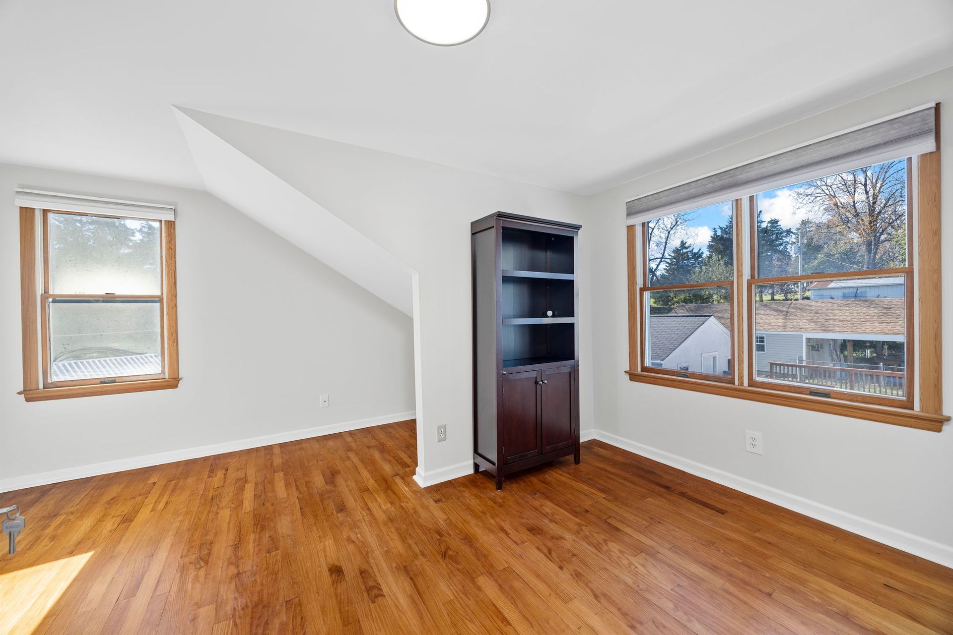 An empty room with hardwood floors and two windows.