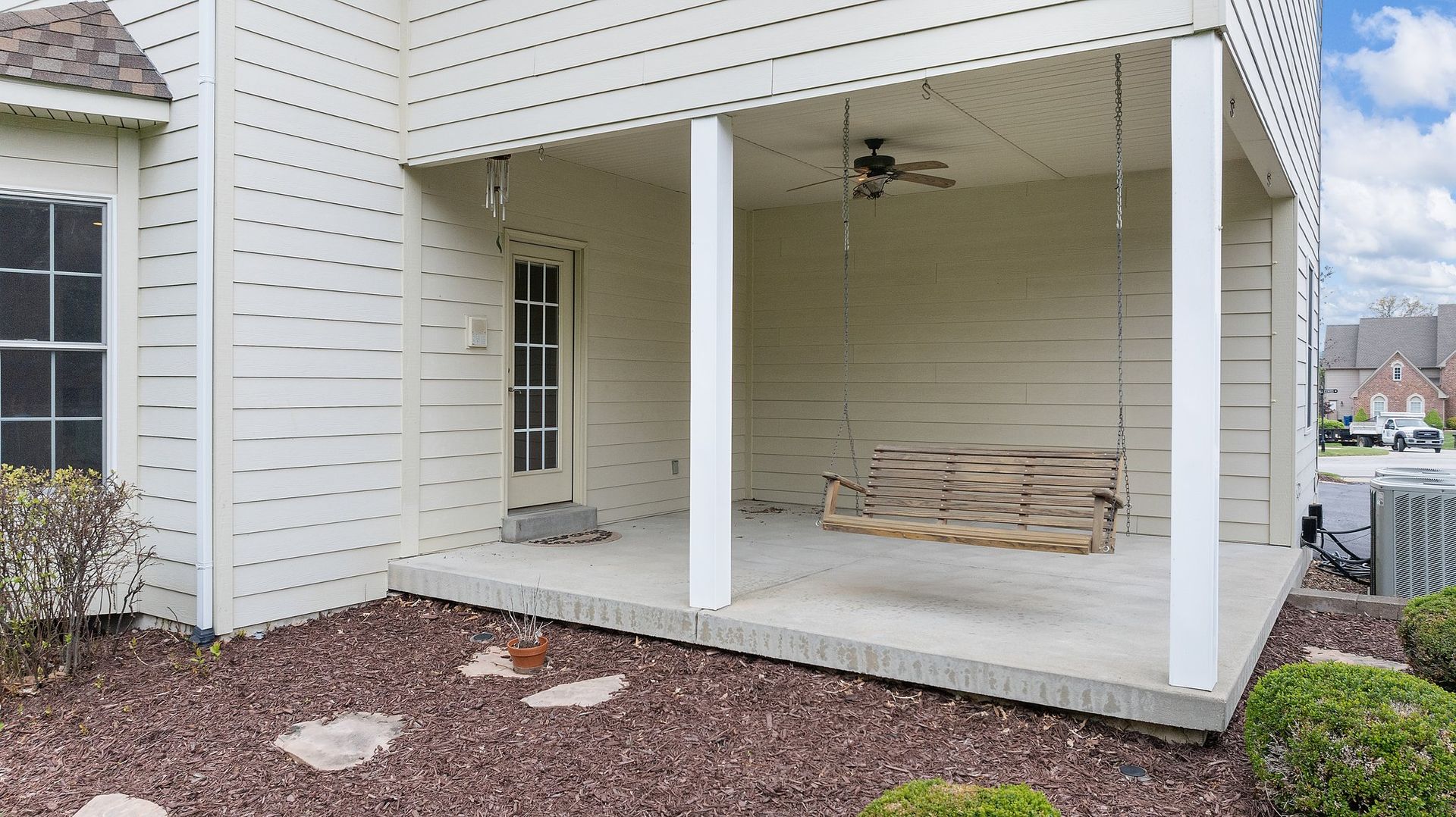 A white house with a porch with a swing and a ceiling fan.