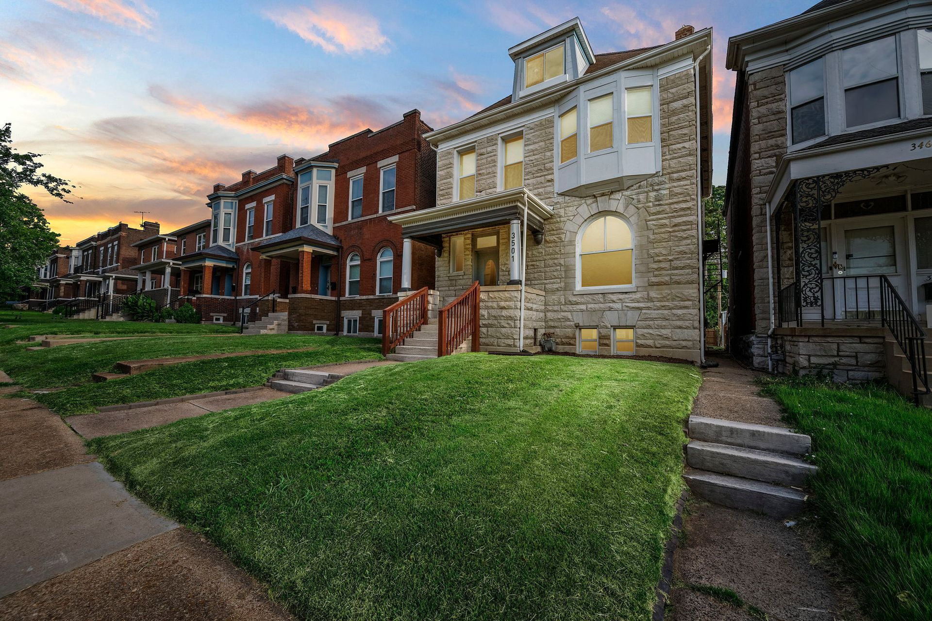 Row of historic brick and stone houses with front lawns, under a sunset sky.
