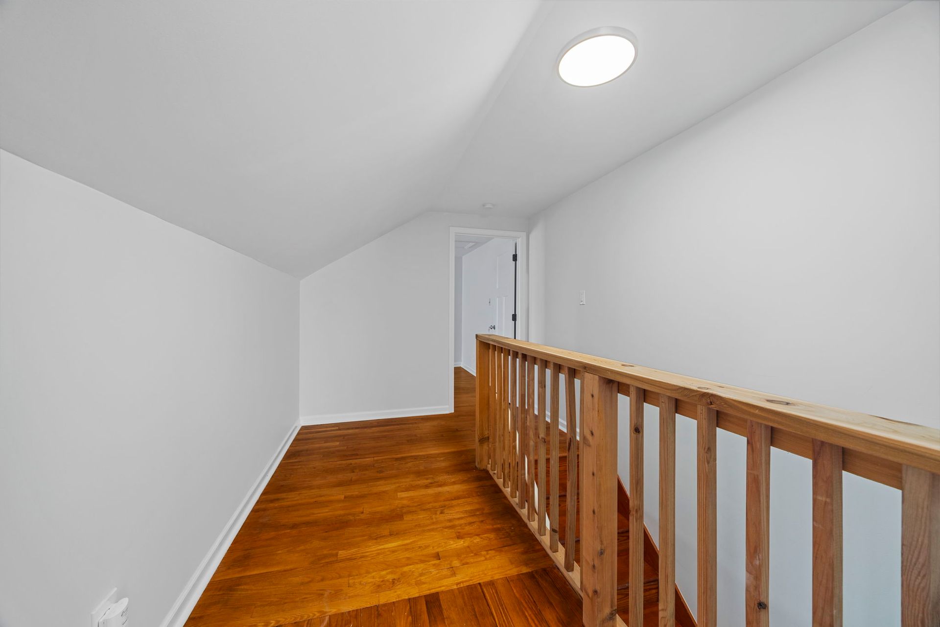 An empty hallway with hardwood floors and a wooden railing leading to the second floor.