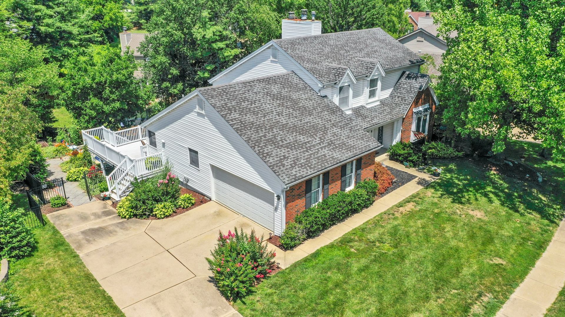 An aerial view of a white house with a gray roof surrounded by trees.