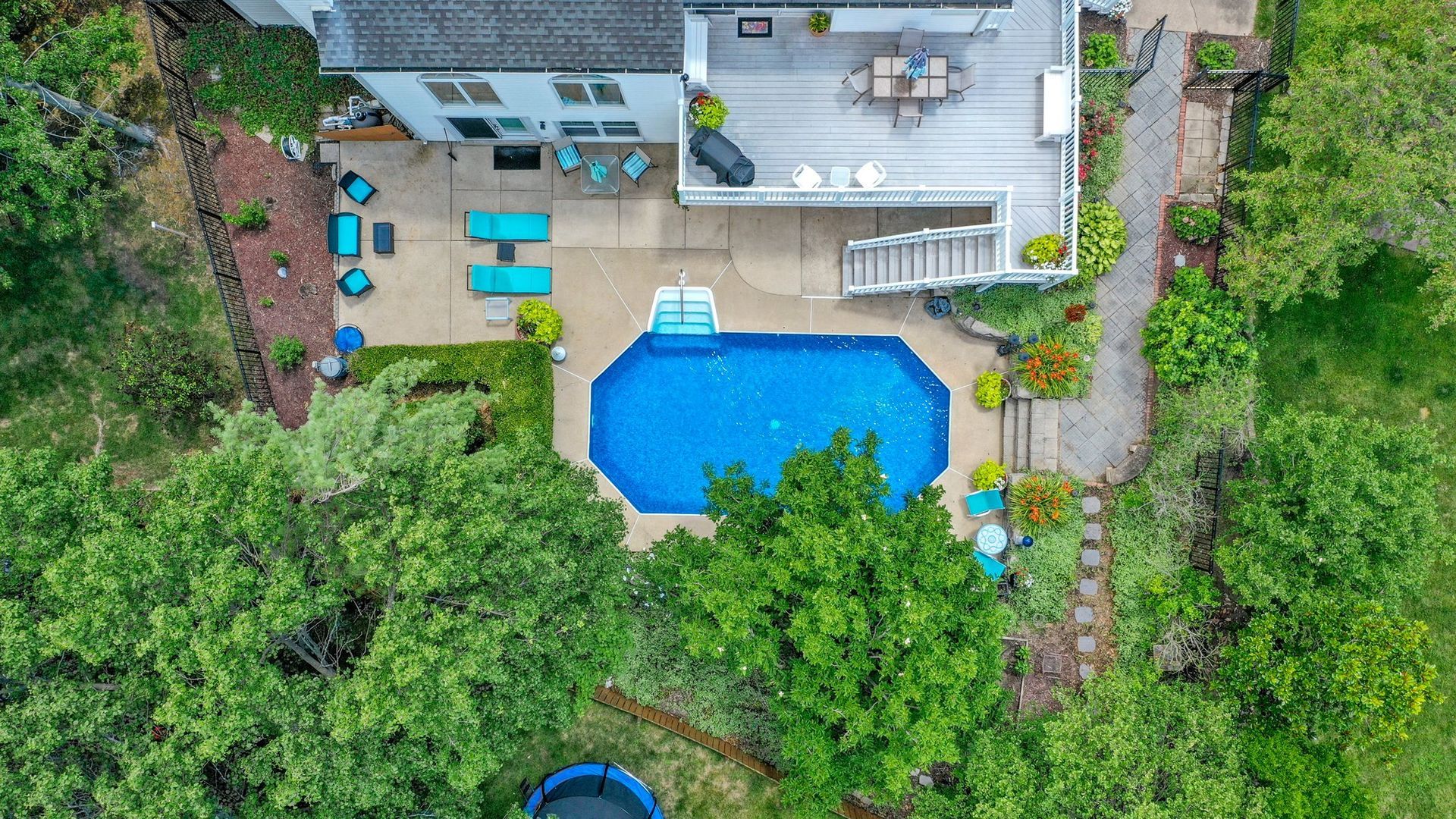 An aerial view of a house with a large swimming pool surrounded by trees.