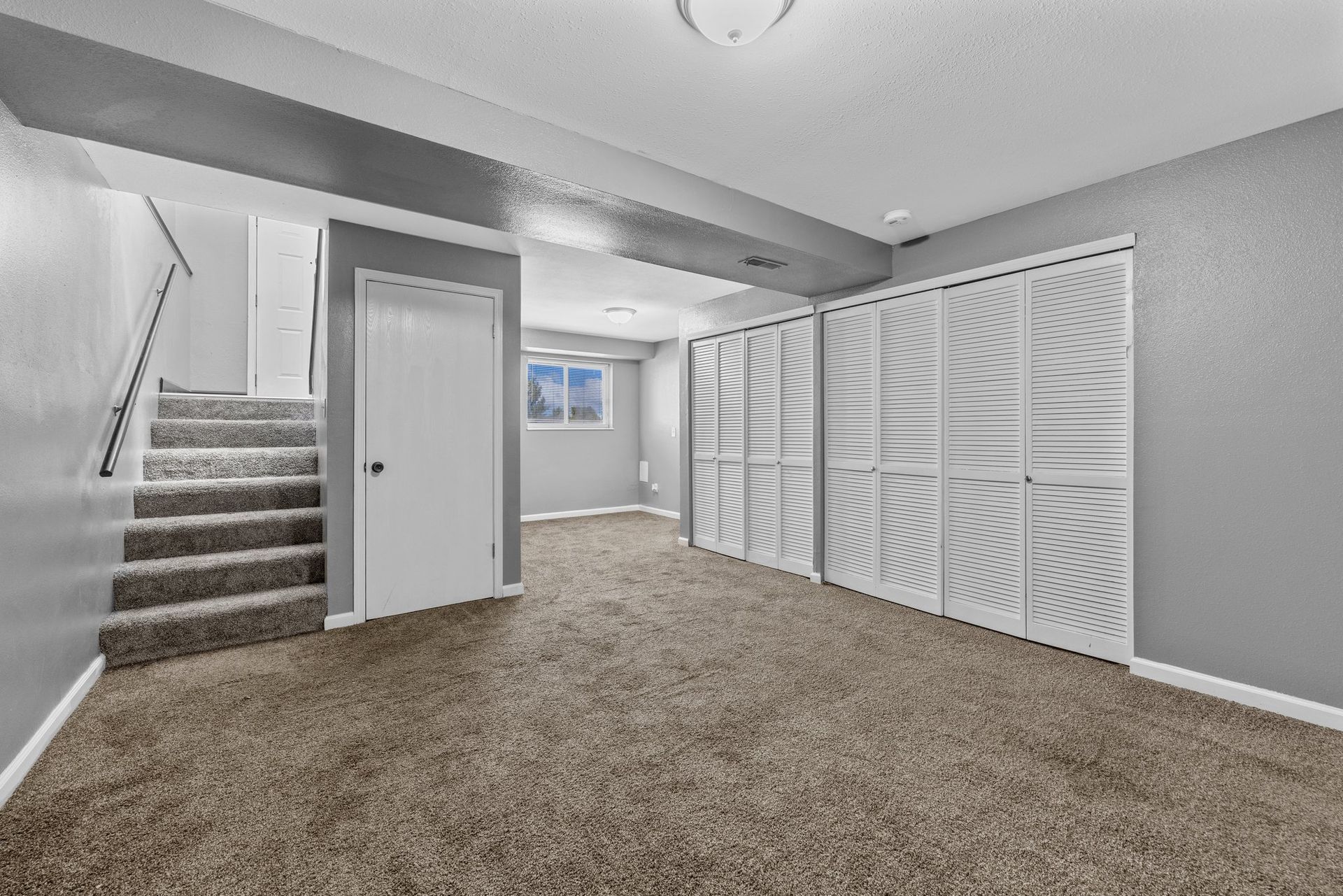 An empty basement with carpeted floors and stairs.