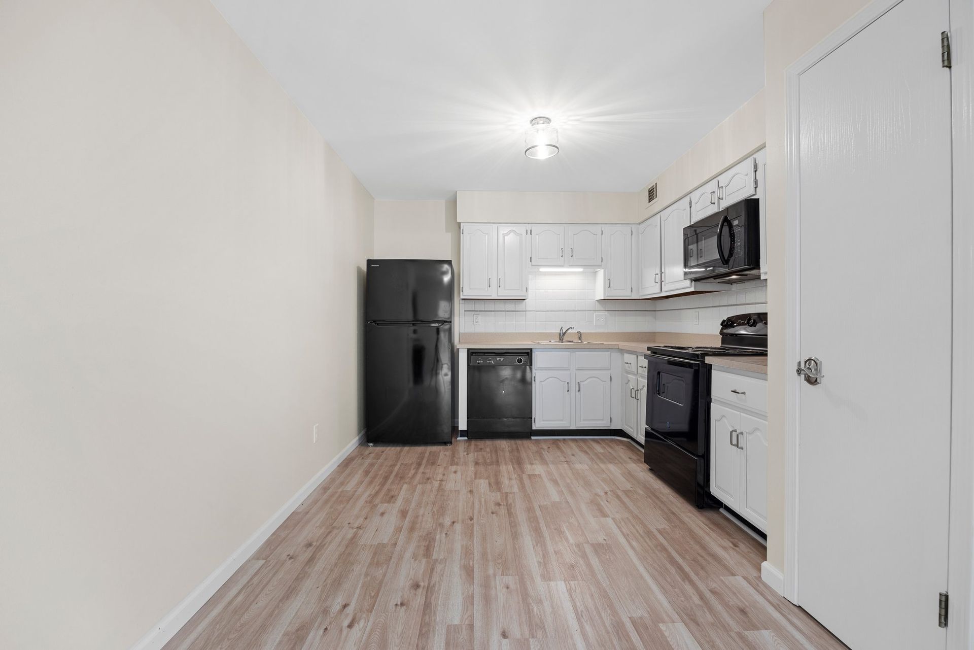 An empty kitchen with white cabinets , a black refrigerator , a black stove , and a microwave.