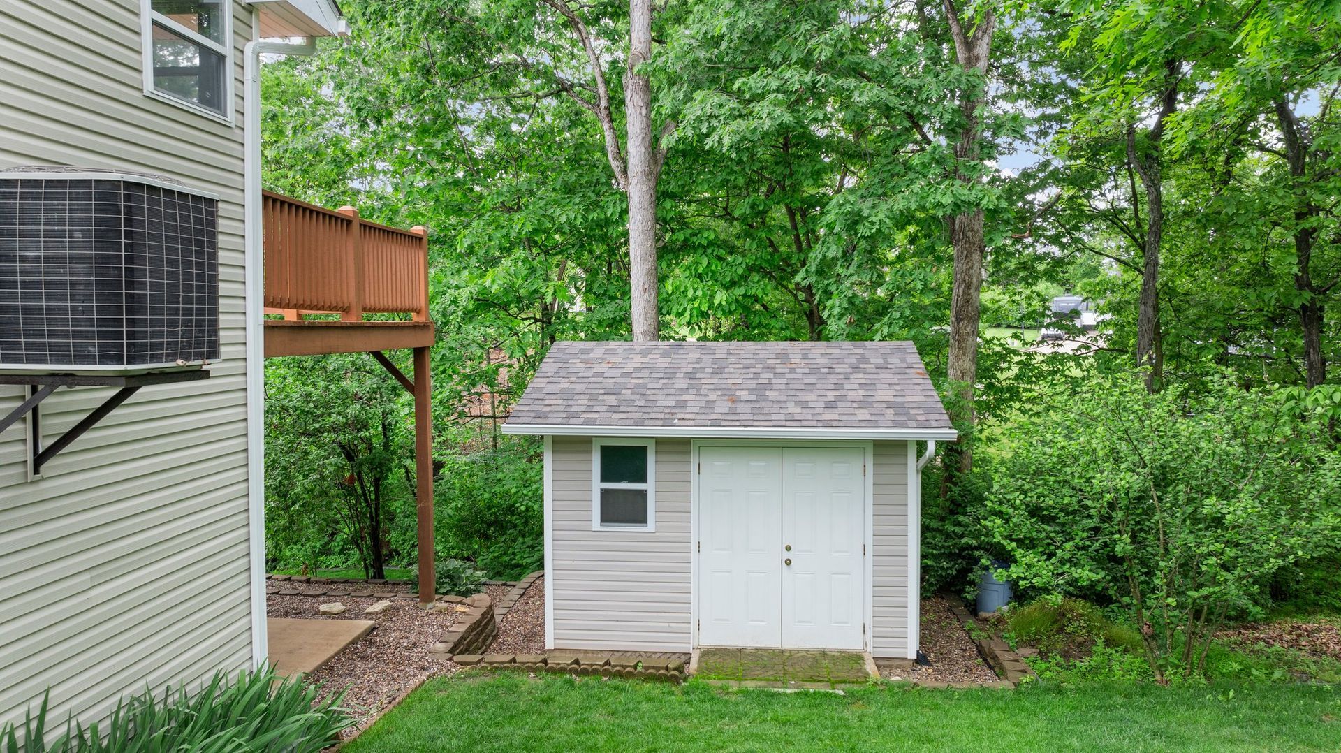 A small white shed is in the backyard of a house.