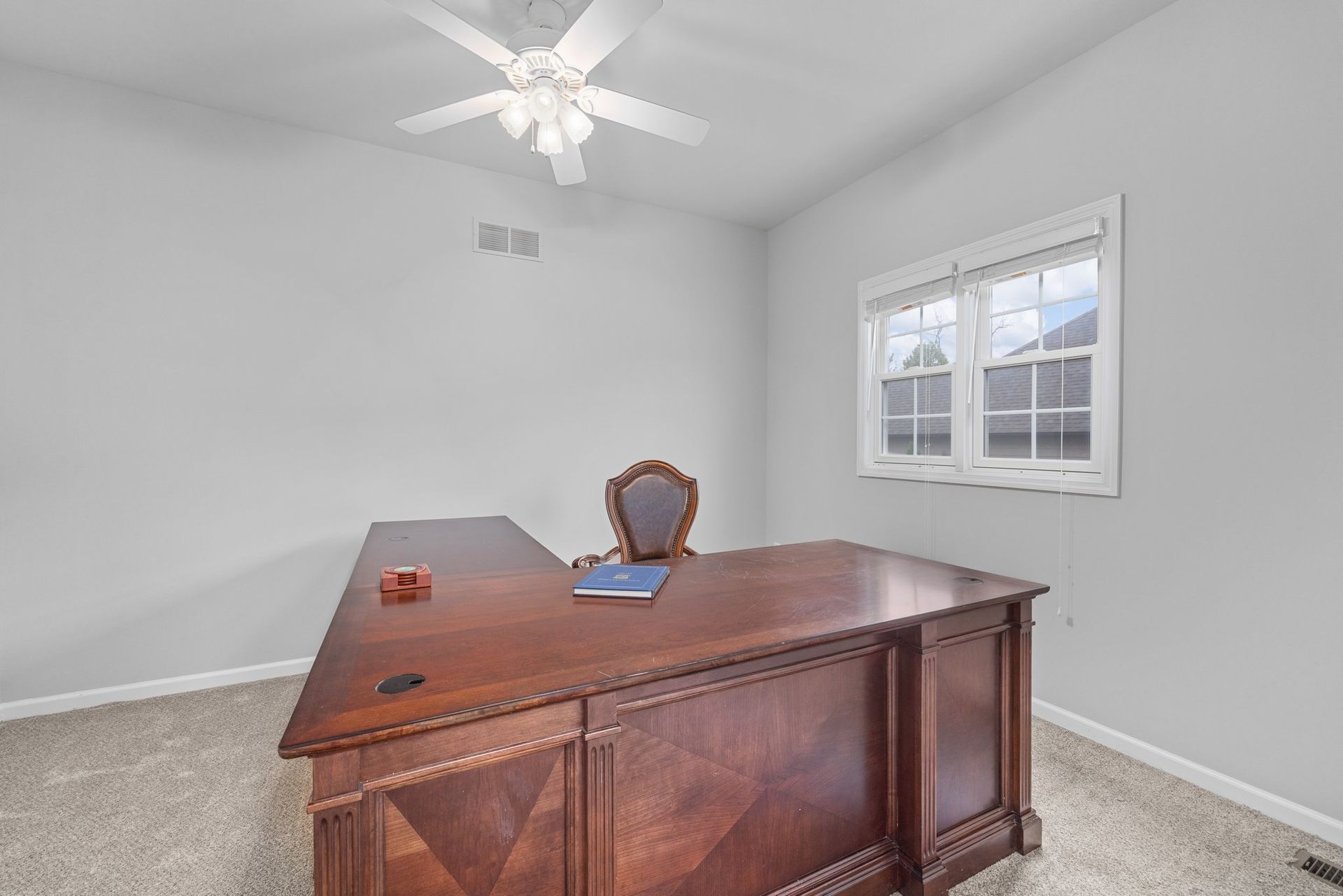 A wooden desk and chair in a room with a ceiling fan.