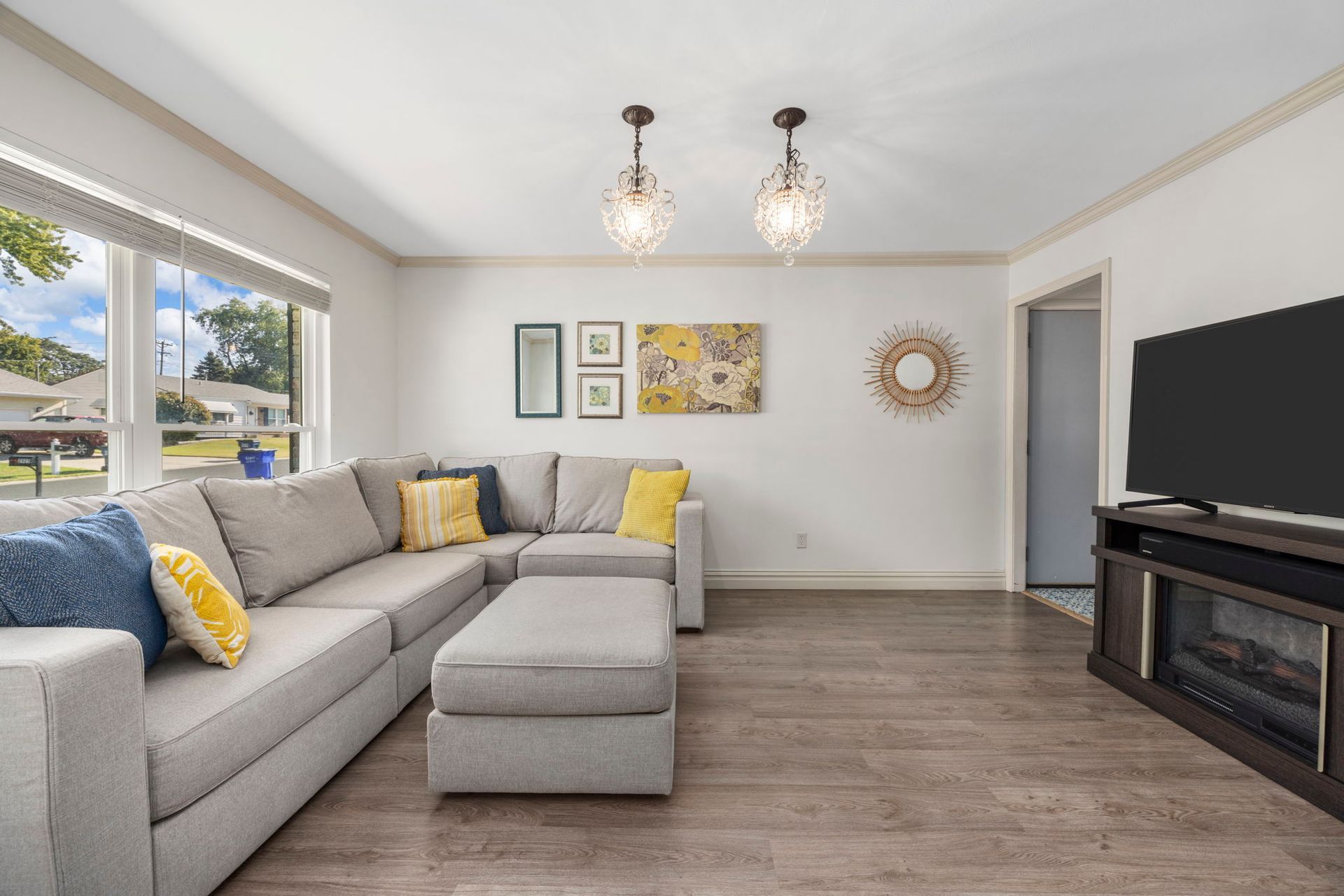 Living room with gray sectional sofa, wooden floor, art, and large TV.