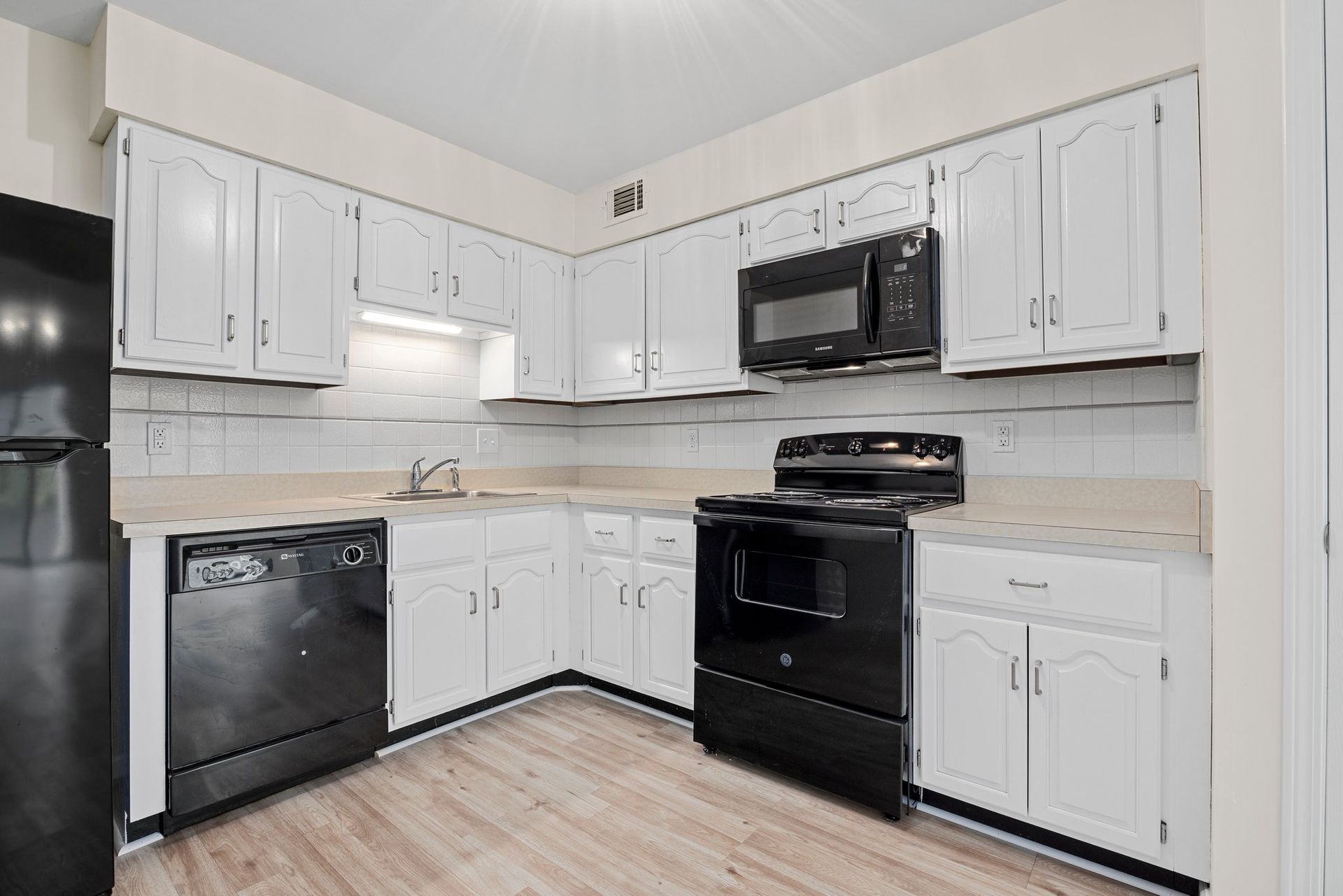 A kitchen with white cabinets , black appliances , and a black refrigerator.