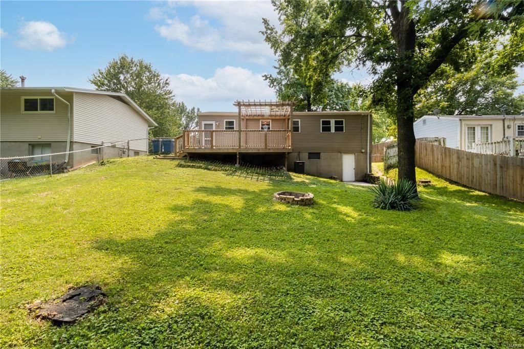 The backyard of a house with a large lawn and a wooden deck.