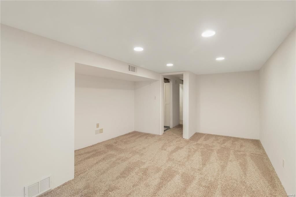An empty basement with white walls and brown carpet.