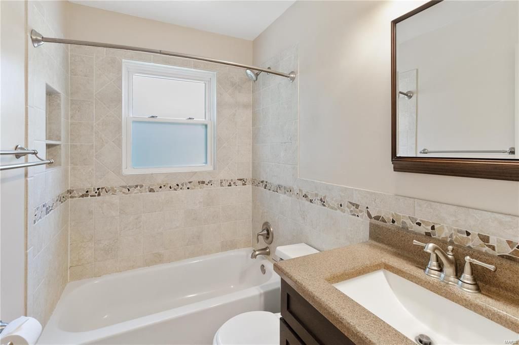 A bathroom with a tub , sink , toilet and mirror.