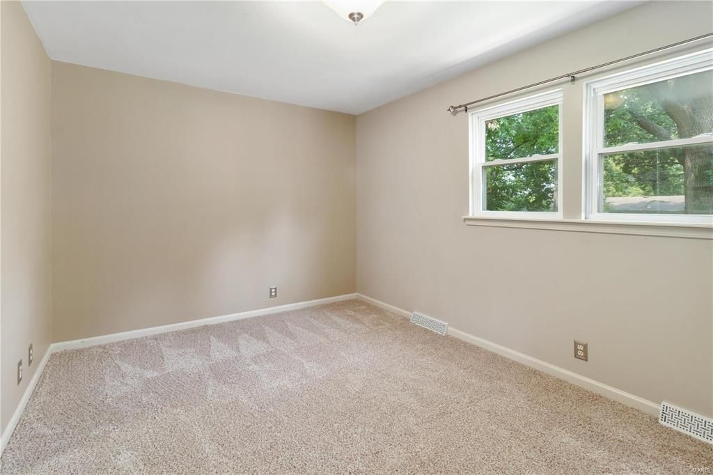 An empty bedroom with a carpeted floor and a window.