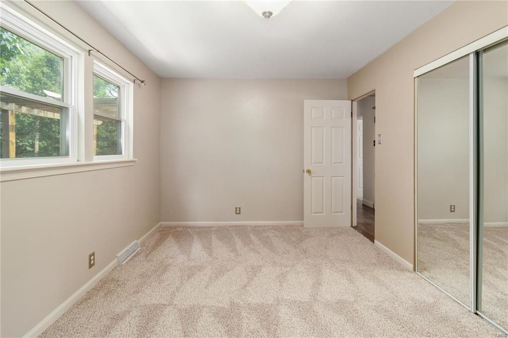 An empty bedroom with a carpeted floor and sliding mirrored doors.