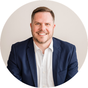 Smiling man in a navy blazer and white shirt, posed against a light gray background