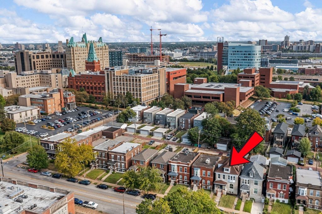 Aerial view of a neighborhood with row houses, the red arrow points to a house with a dark roof.