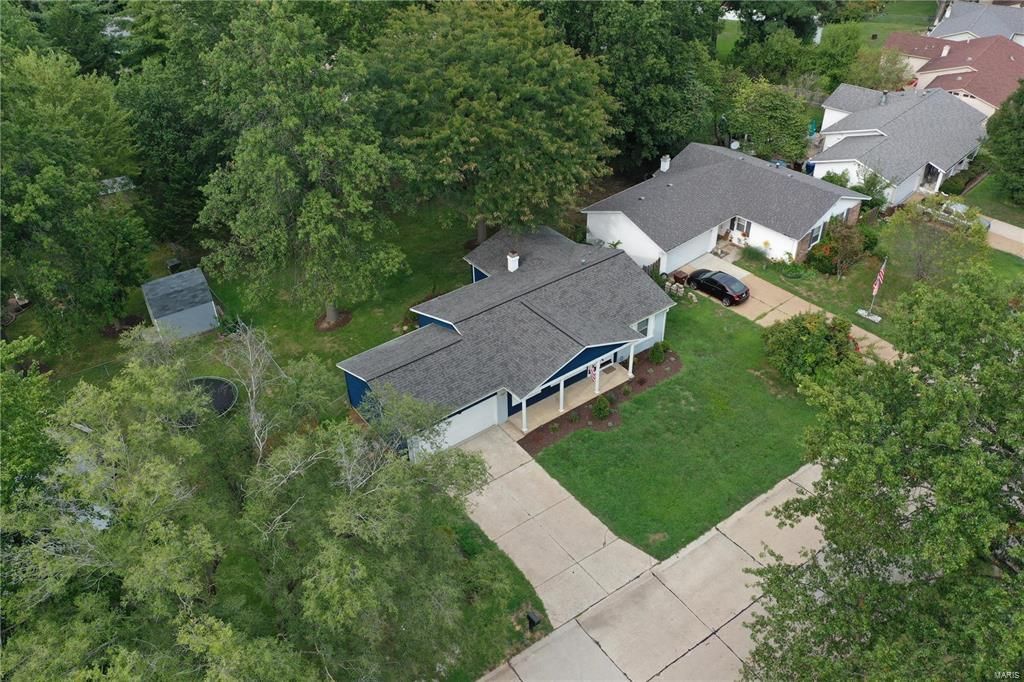 An aerial view of a house in a residential area surrounded by trees.