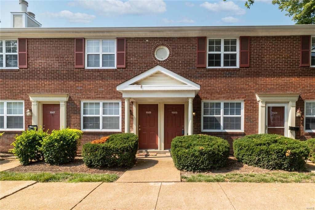 The front of a brick apartment building with a walkway leading to it.