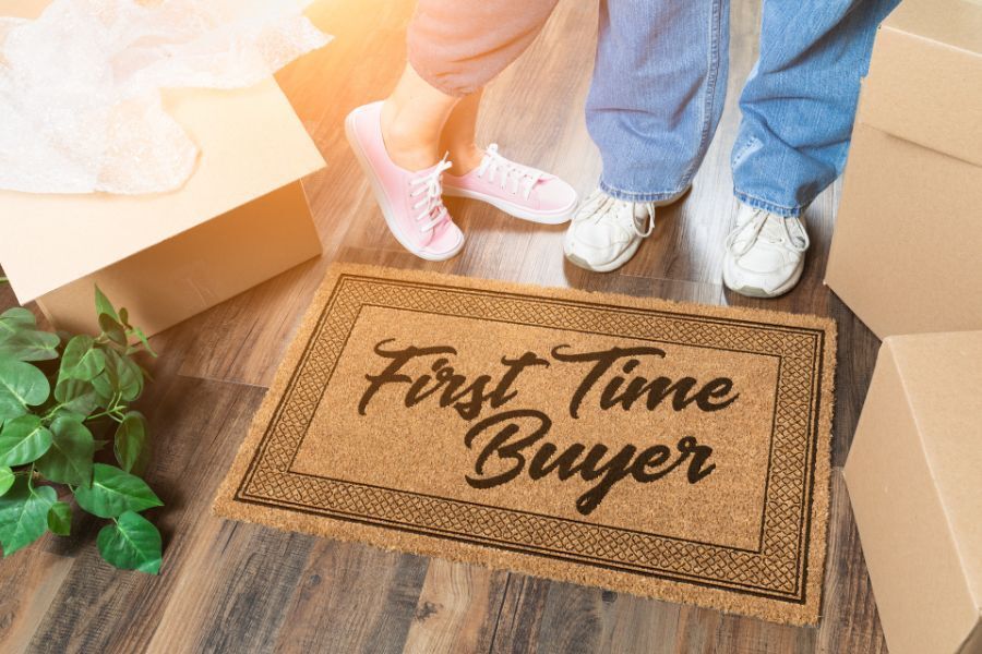 A couple is standing next to a welcome mat that says `` first time buyer ''.