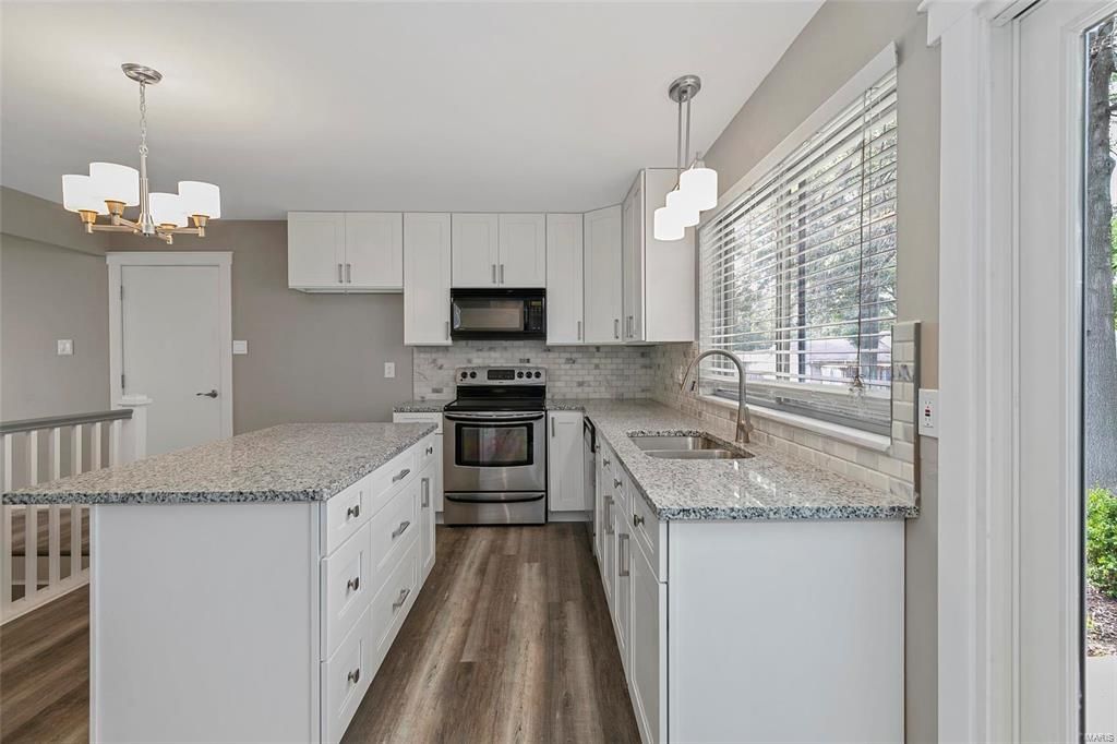 A kitchen with white cabinets , granite counter tops , stainless steel appliances and a large island.