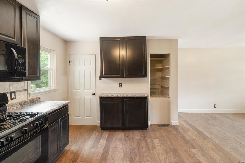 An empty kitchen with black cabinets and a stove top oven.