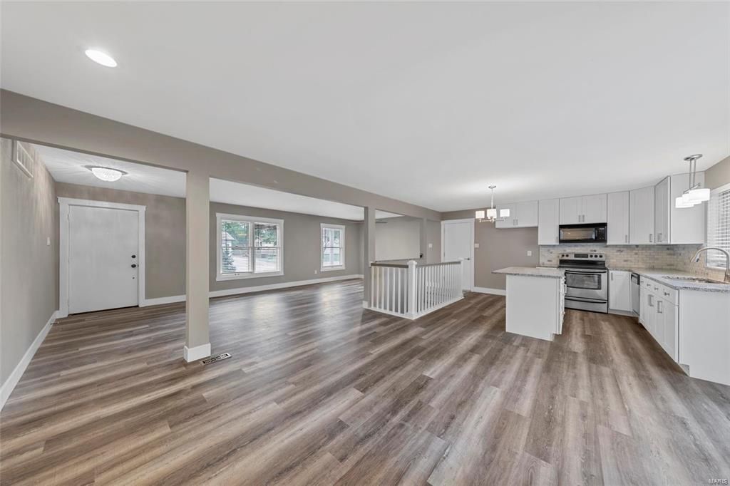 A large empty room with hardwood floors and a kitchen.