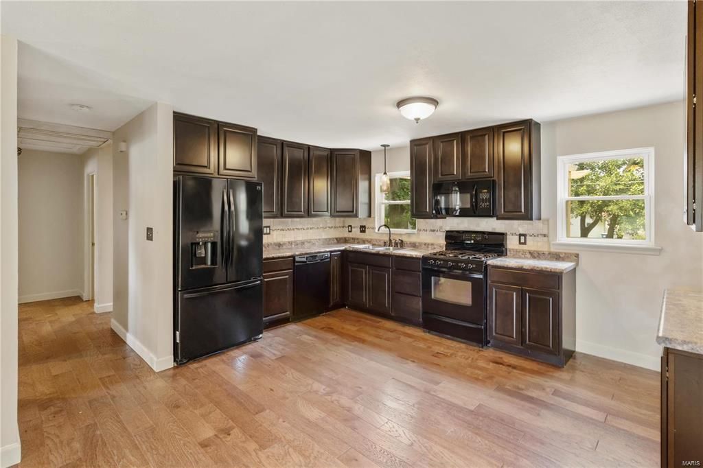 A kitchen with brown cabinets , black appliances , and hardwood floors.