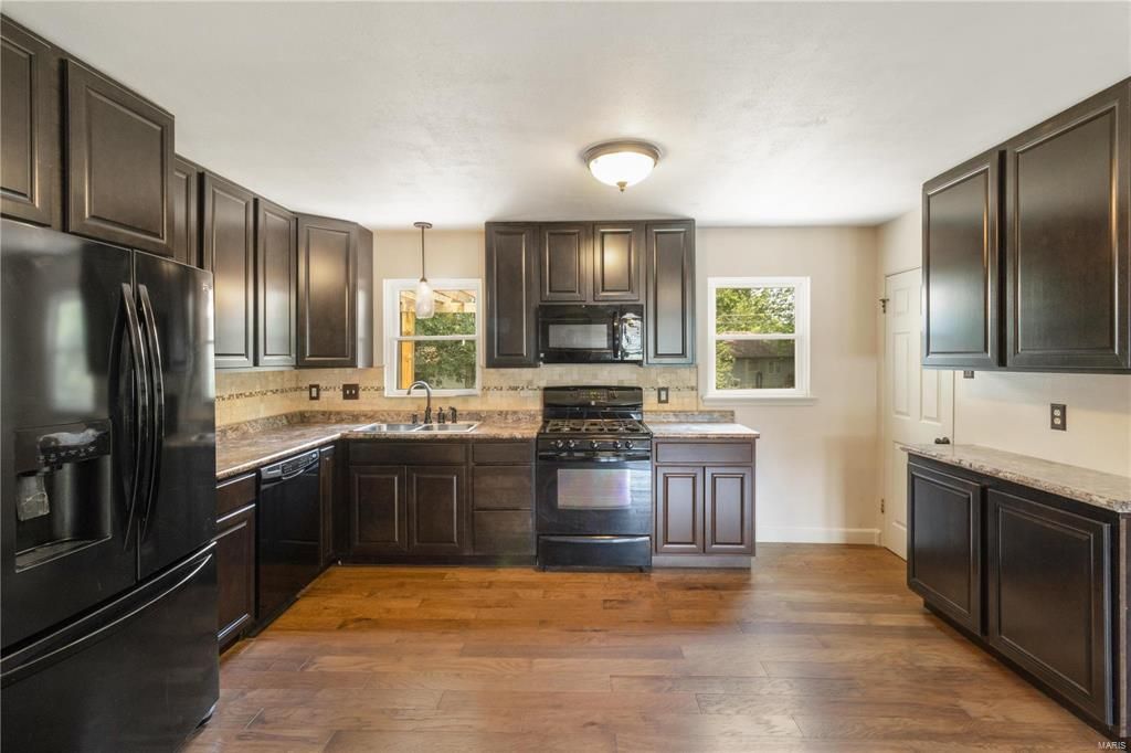 A kitchen with black cabinets , stainless steel appliances , and hardwood floors.