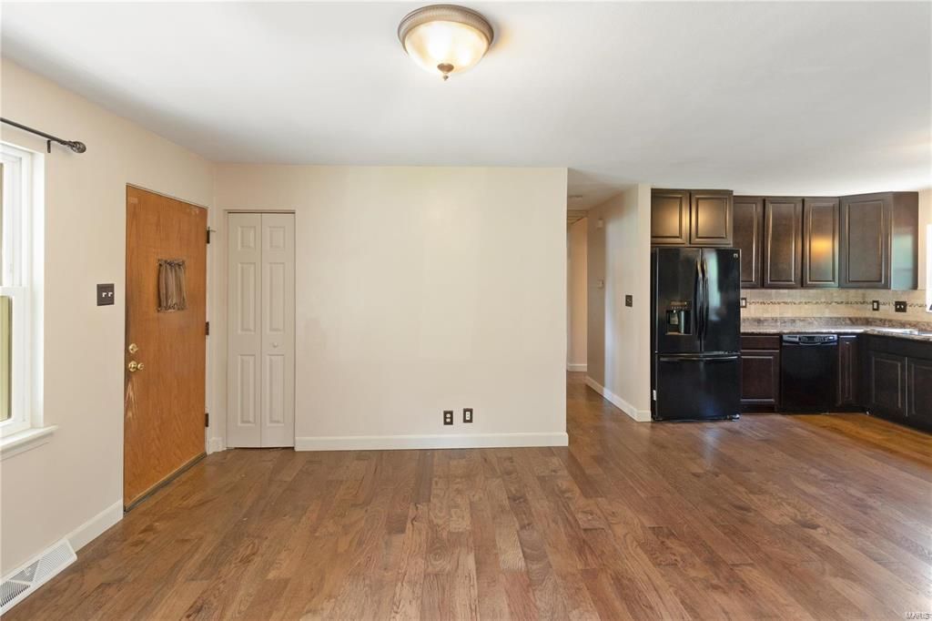 A living room with hardwood floors and a kitchen in the background