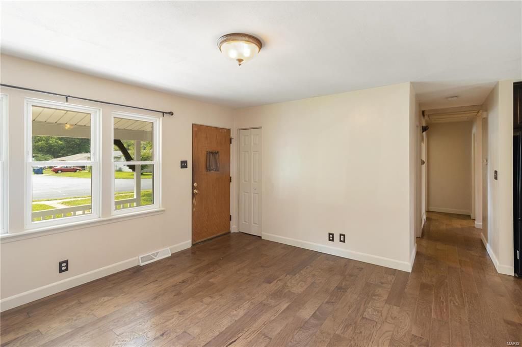 An empty living room with hardwood floors and a wooden door.