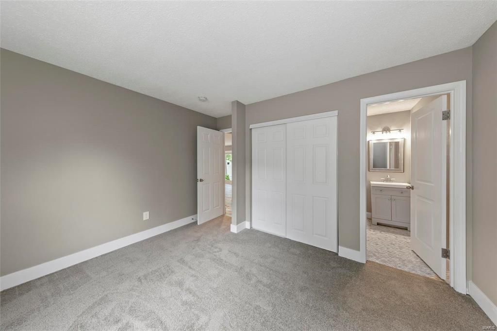 An empty bedroom with a carpeted floor , closets and a bathroom.