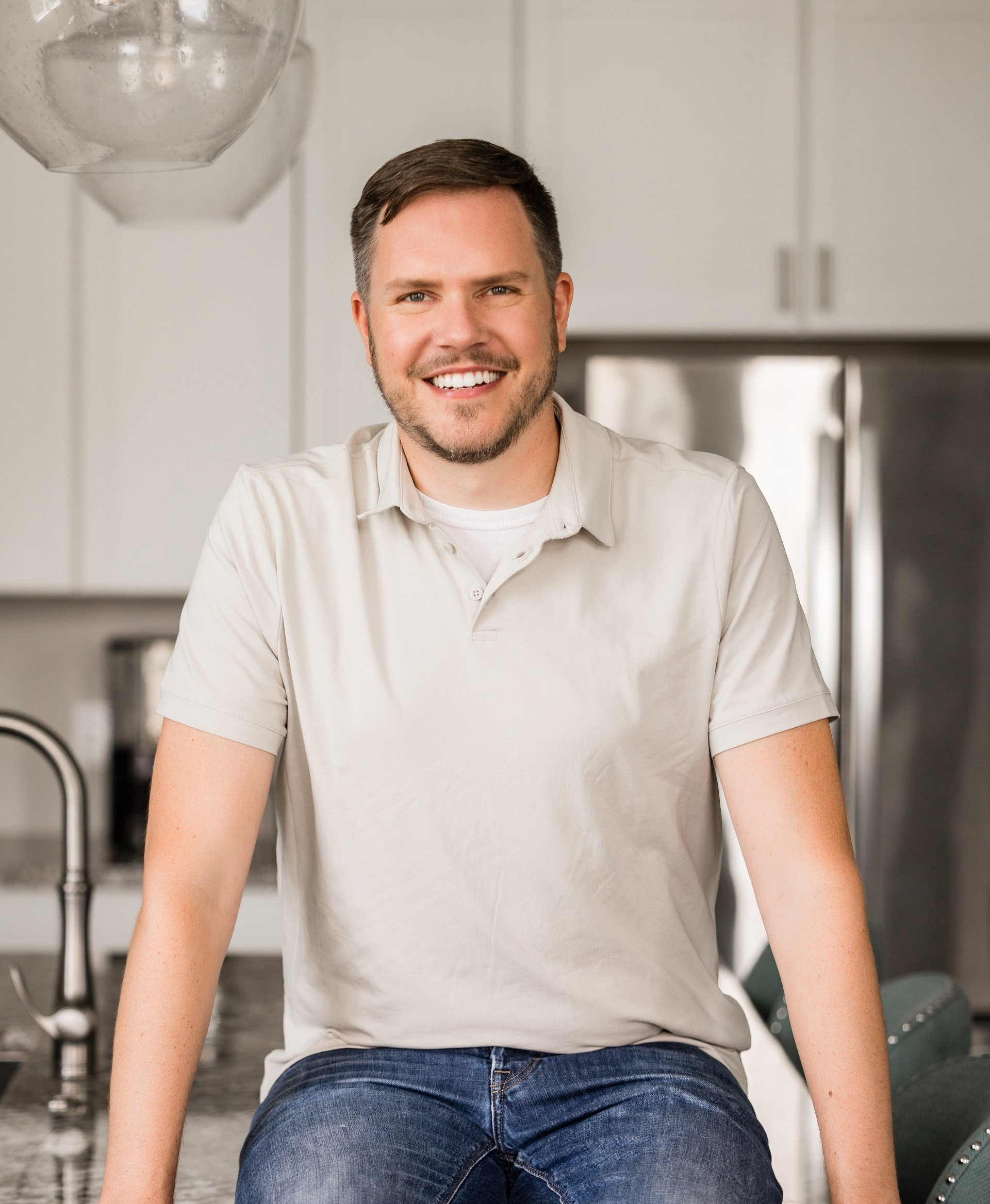 A man is sitting on a counter in a kitchen smiling at the camera.