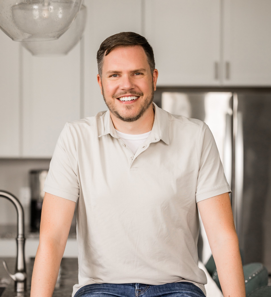 A man in a white shirt is sitting on a counter in a kitchen.