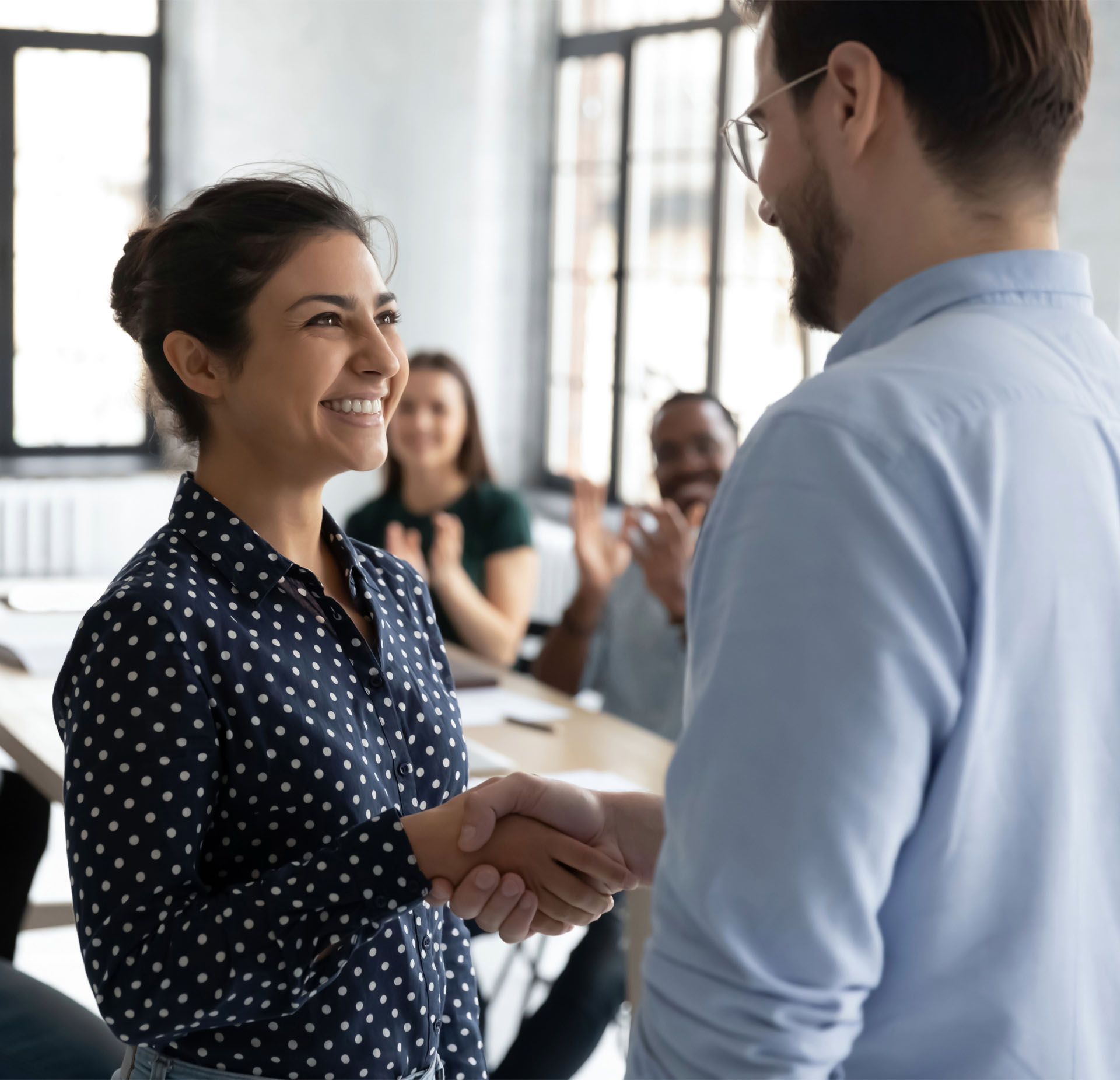 A man and a woman are shaking hands in an office.