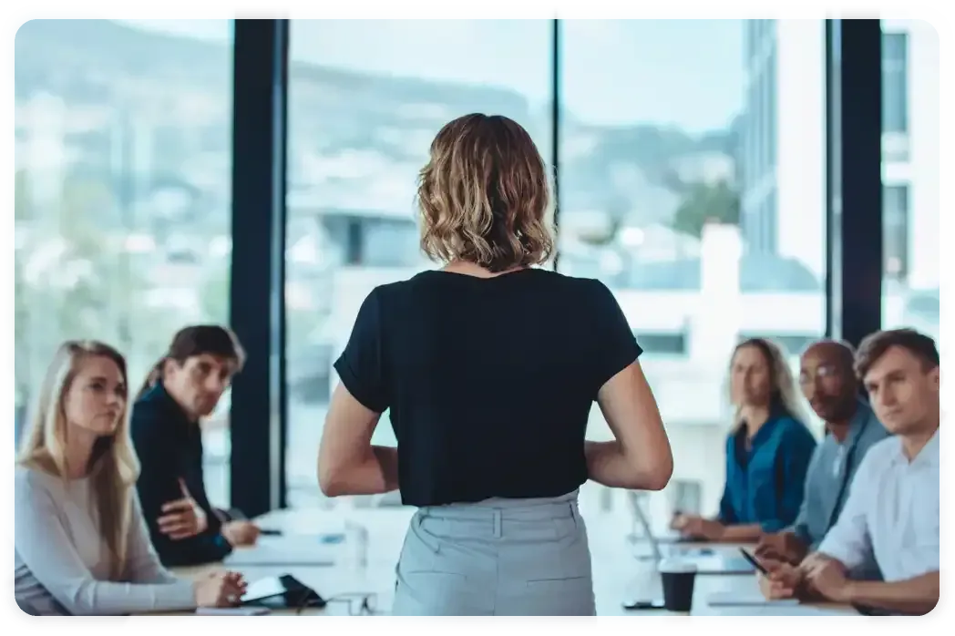 A woman is giving a presentation to a group of people sitting around a table.