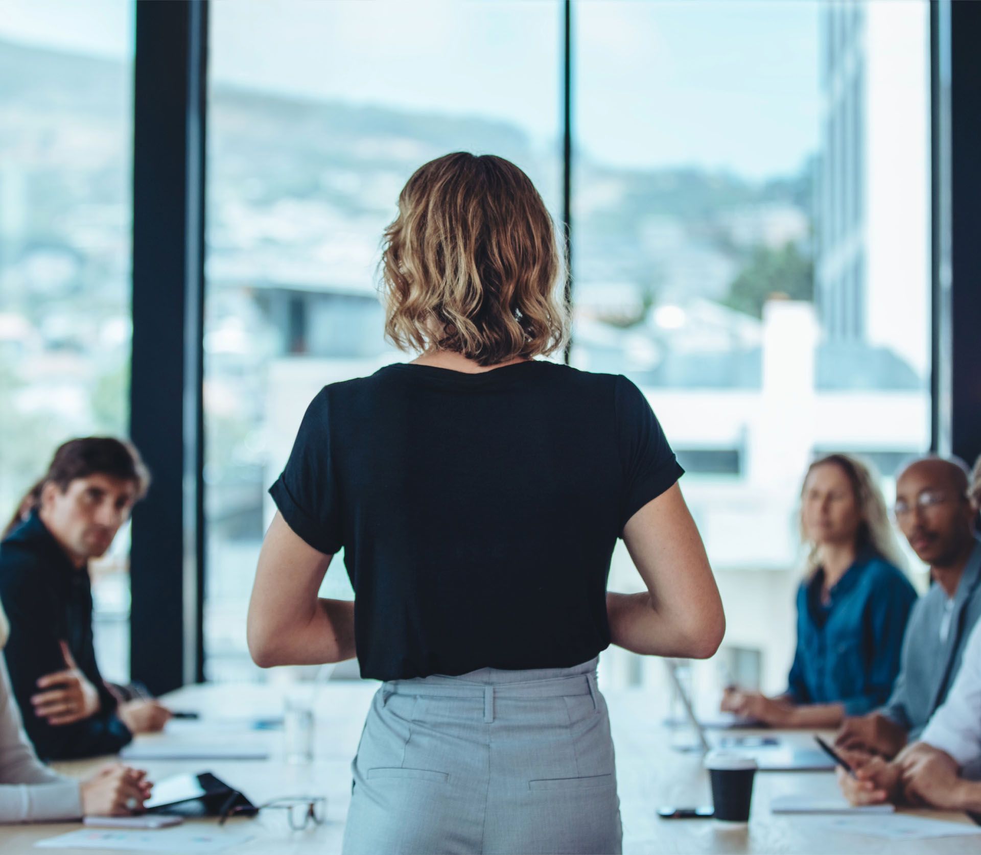A woman is giving a presentation to a group of people sitting around a table.