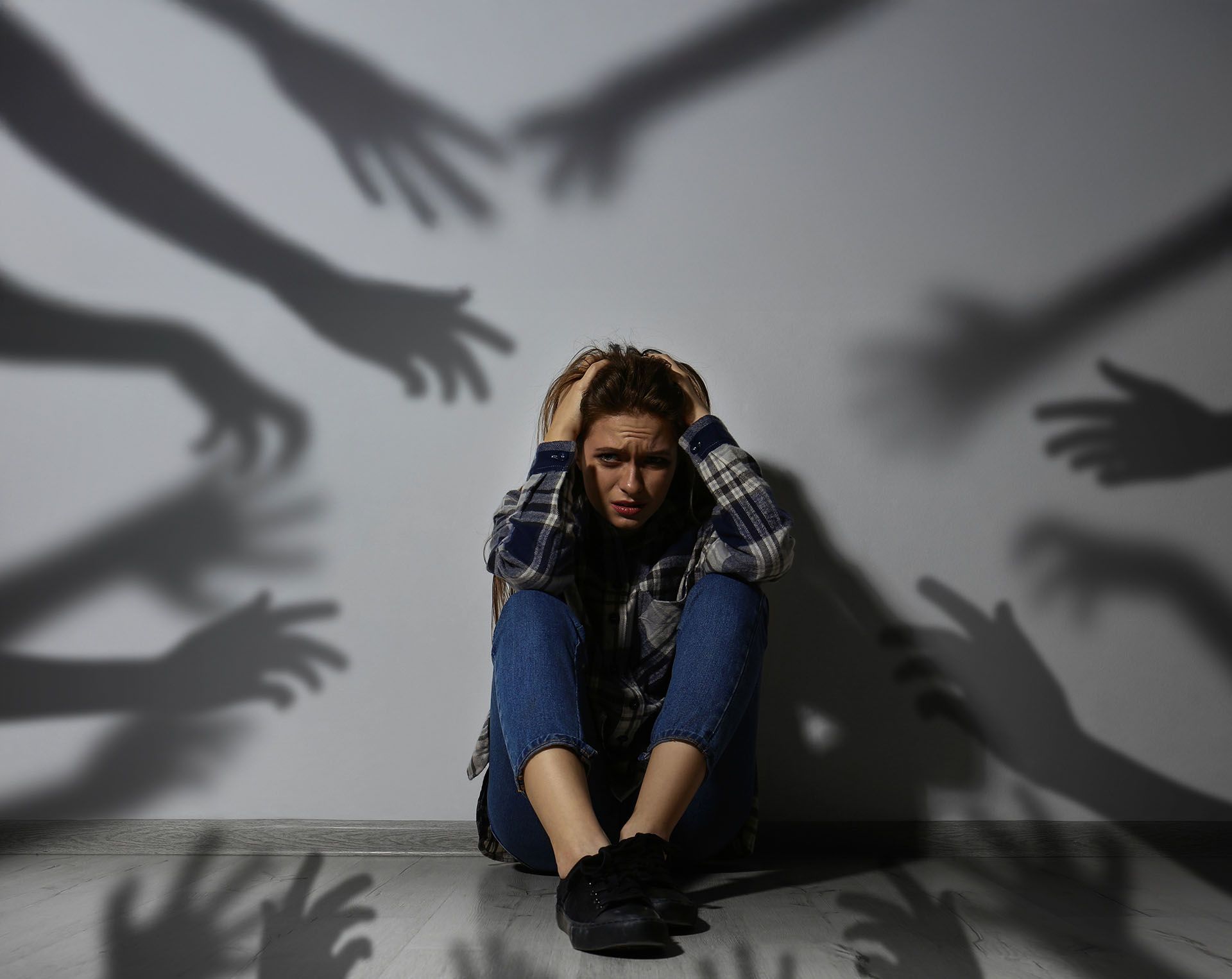 A woman is sitting on the floor surrounded by shadows of hands.