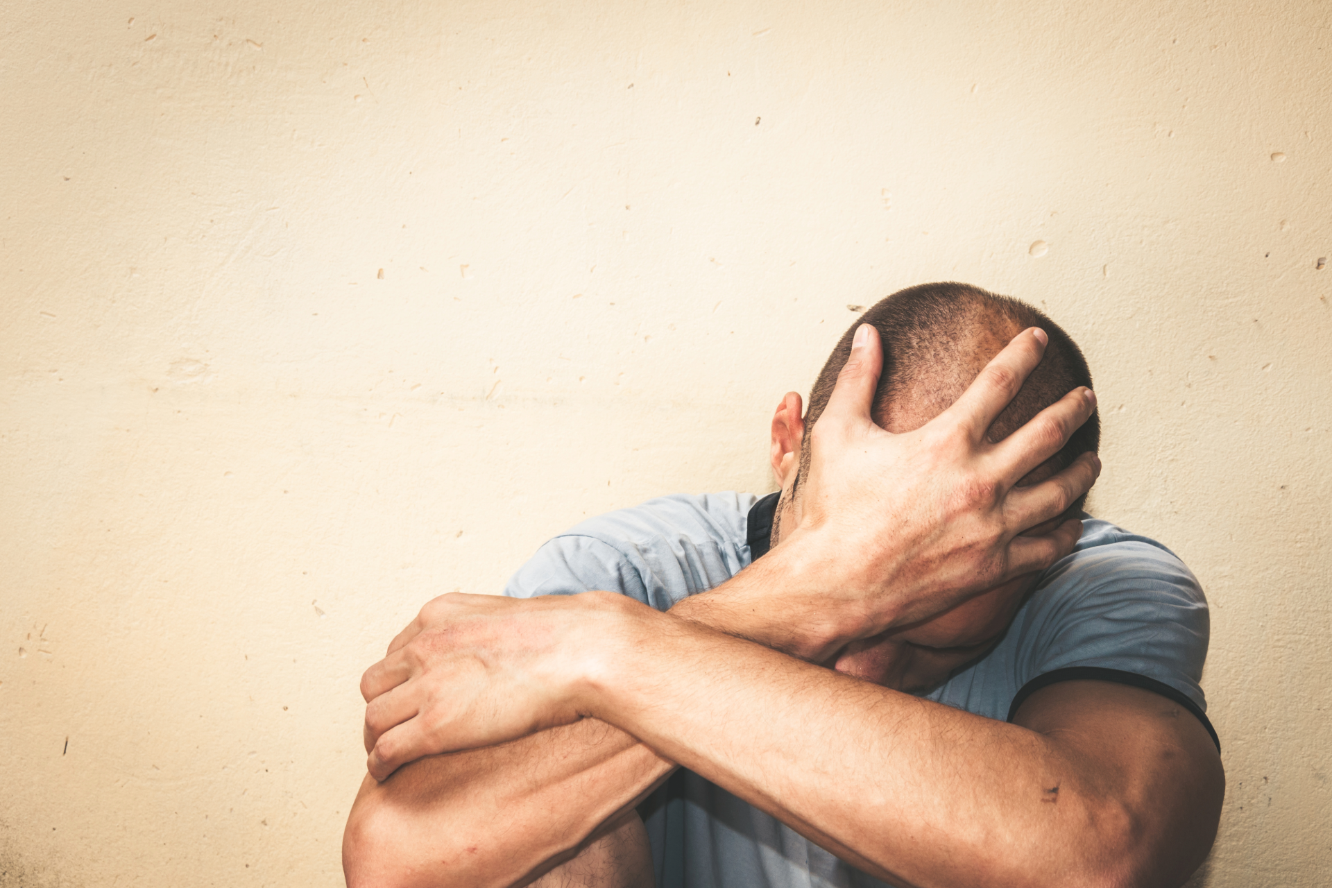 Person sitting against a wall with head in hands and arms crossed, appearing distressed