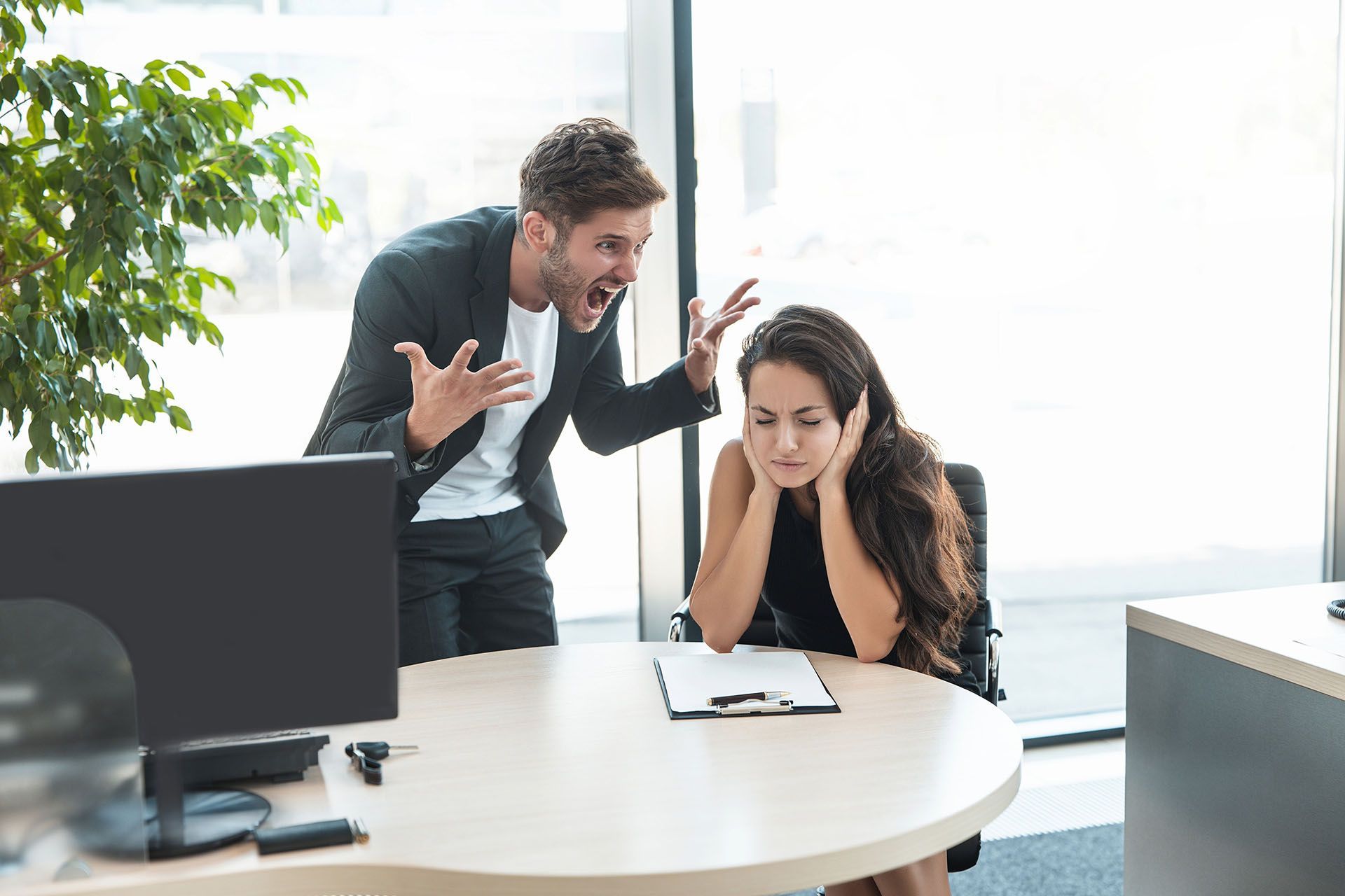 Man yelling, woman covering ears in an office.
