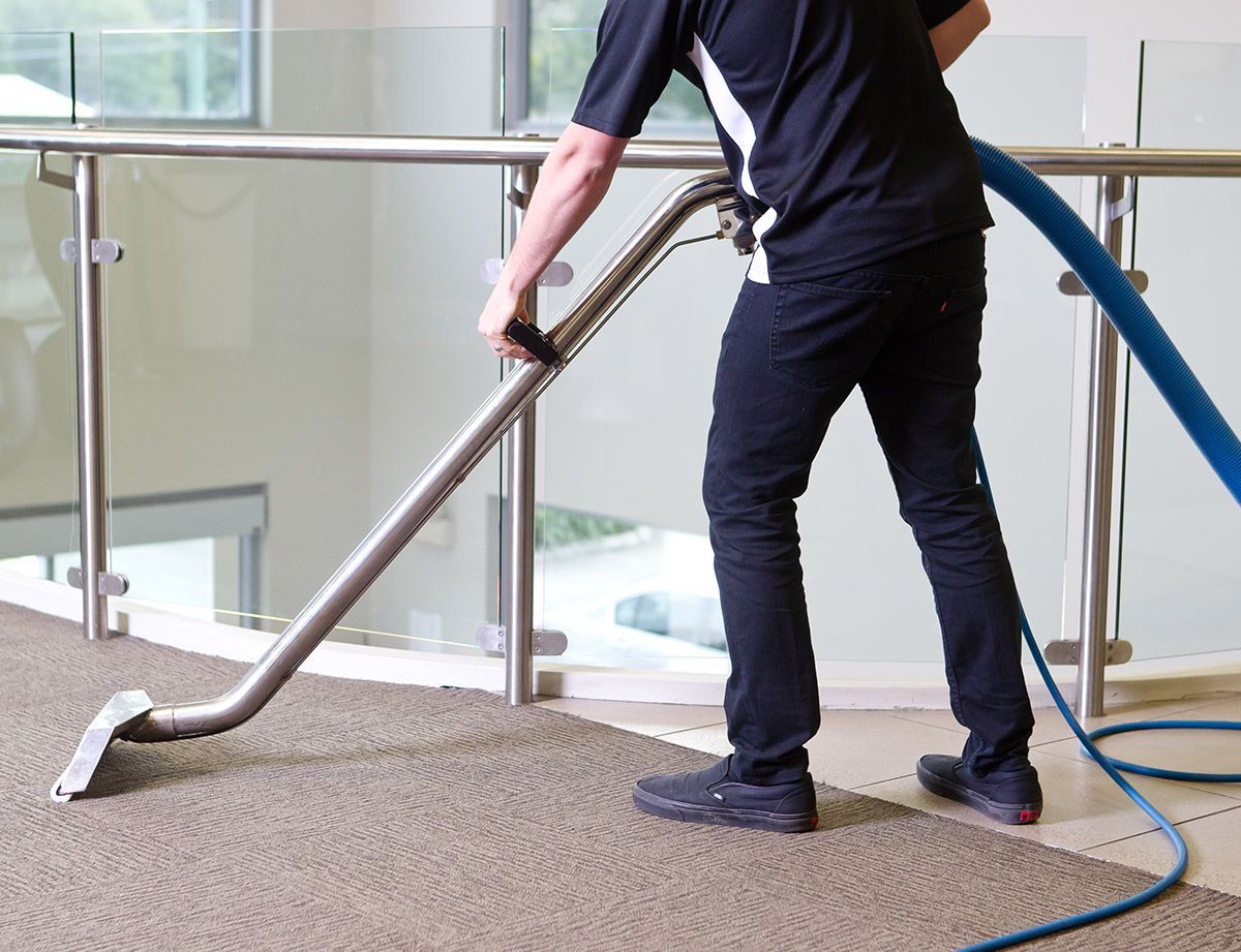 A man is cleaning the floor of an office with a vacuum cleaner.