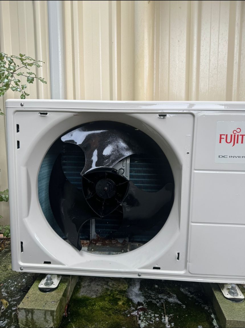 White Fujitsu air conditioning unit with black fan, mounted outside.